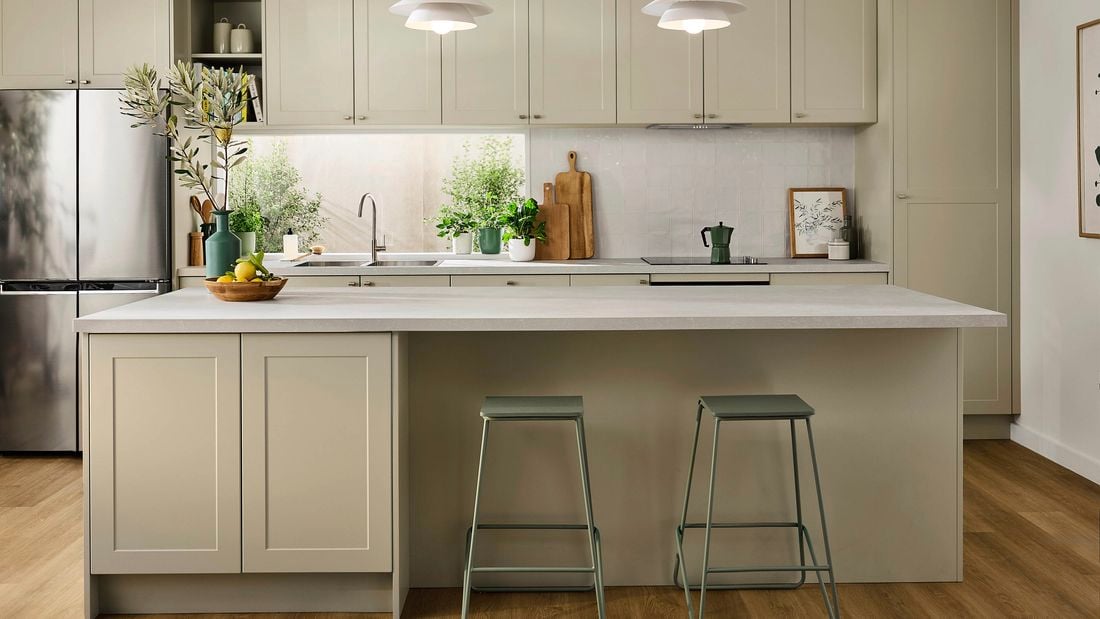 A modern New Rural kitchen featuring soft sage green shaker cabinets, light stone benchtops, timber flooring, and potted greenery for a fresh, natural look