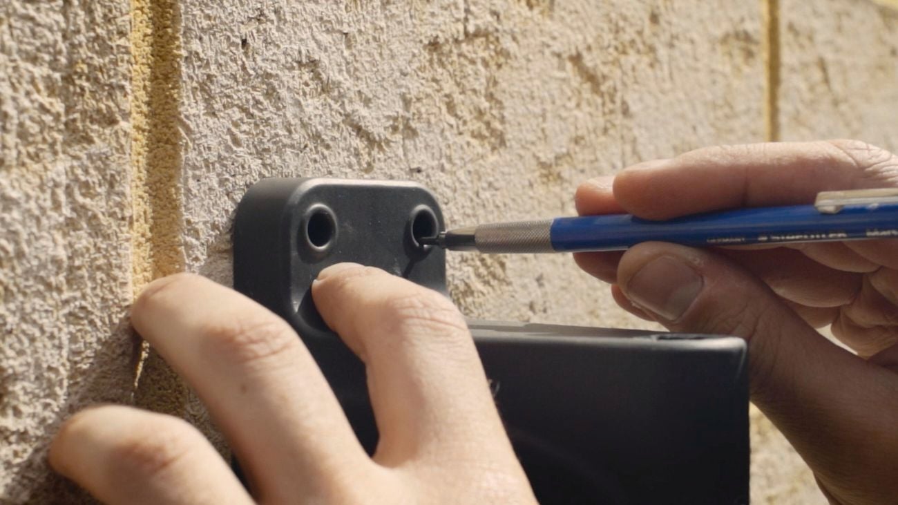 Pair of hands using a pencil to mark a brick wall with drill holes