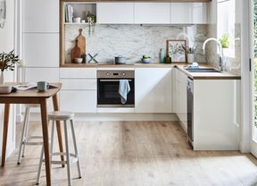 A Scandi kitchen with white cabinets, a marble splashback, and a wooden bench and stools.