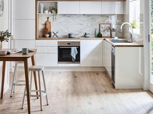 A Scandi kitchen with white cabinets, a marble splashback, and a wooden bench and stools.