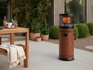 Rustic new outdoor patio heater sitting in a lovley patio area surrounded by green shrubs and outdoor setting