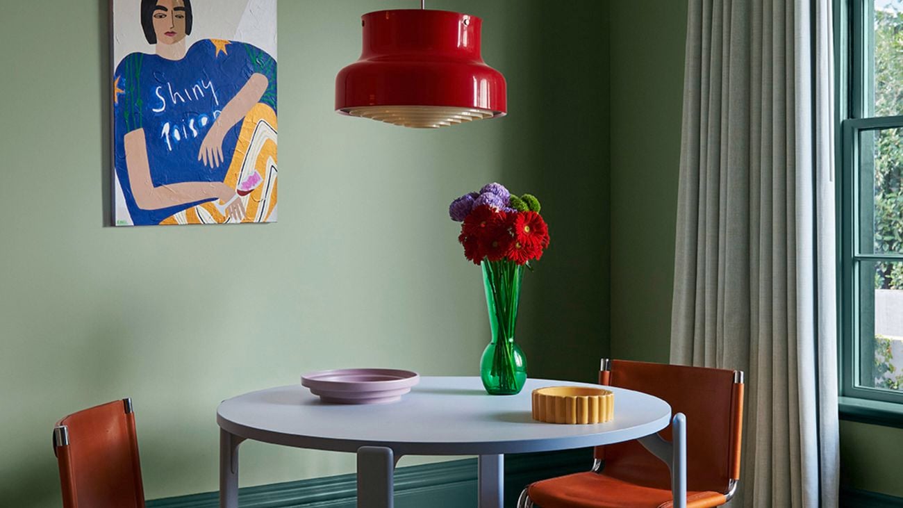 A dining room with light green walls, a dining table with chairs on orange carpet.
