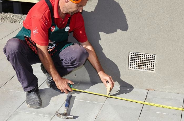 A person measuring a distance on pavers and inserting a wedge between two pavers