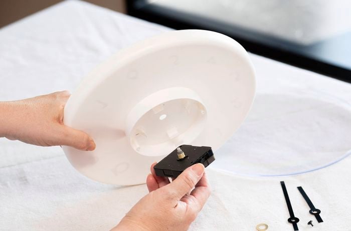 A person is removing the clock mechanism from a wall clock while preparing it for a DIY upcycle project.