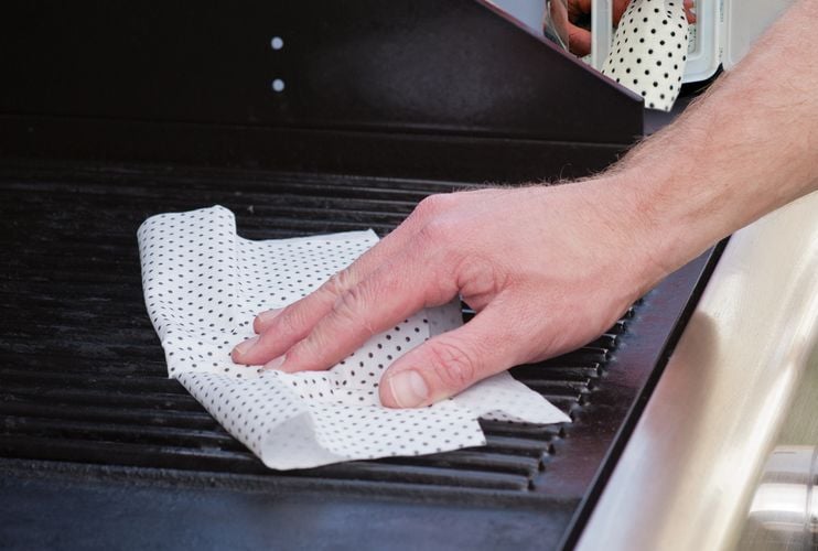 Person cleaning barbecue with wipe
