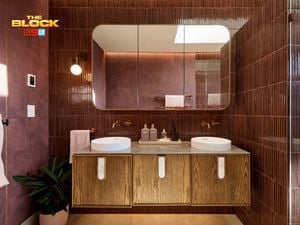 Modern bathroom with double round sinks on a wooden vanity, large mirror, maroon tiled walls, and partial view of a glass shower. 