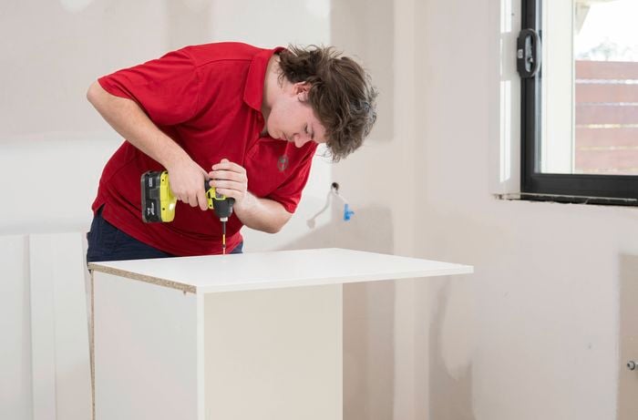 A Bunnings Team Member is using a power drill to fix the side panels to the base and back.