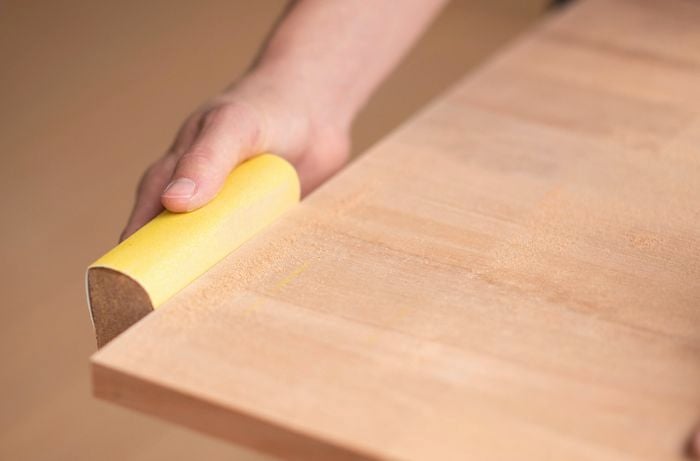A hand is using a sanding block to smooth out any rough edges on the benchtop. ]