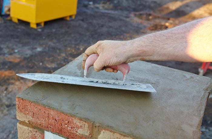 Cement on top of a brick mailbox being smoothed out with a trowel