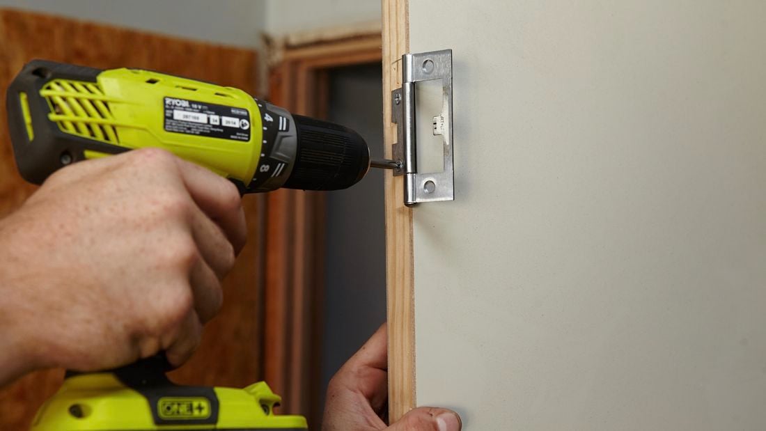 A door hinge being screwed into a doorframe using a power drill
