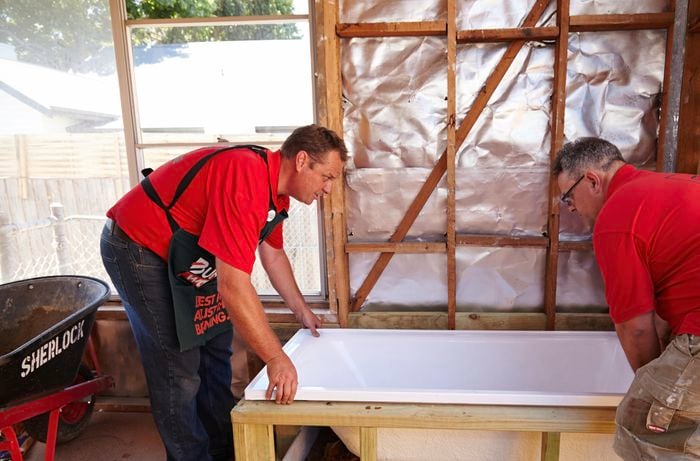 Two people placing a bath into the timber bath frame they just made.