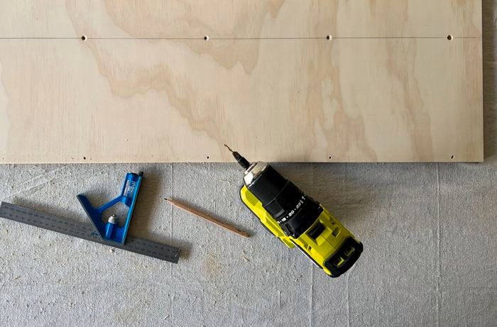 rectangular piece of wood with five evenly drilled holes sitting beside a drill and metal ruler