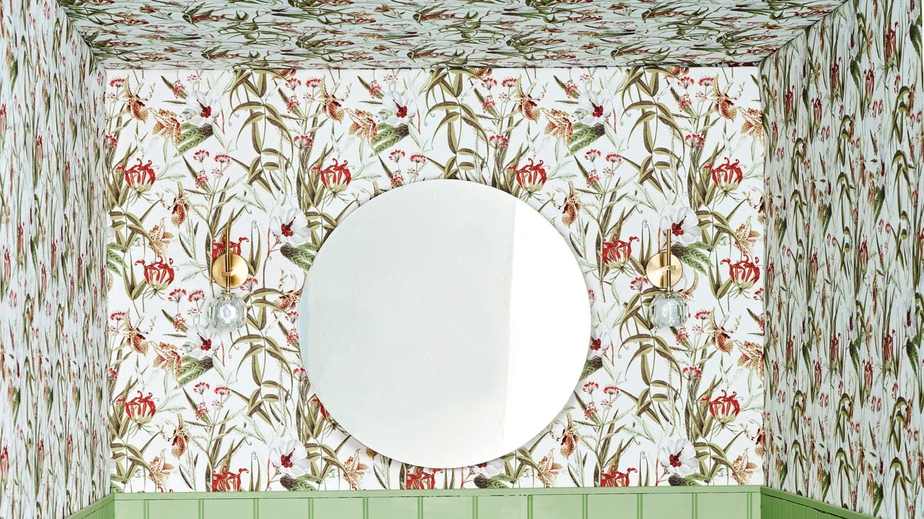 Green powder room with patterned wallpaper and black and white tiled flooring.