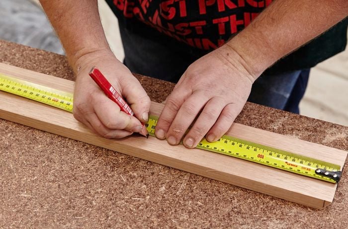 A person marking a piece of timber with a pencil and measuring tape