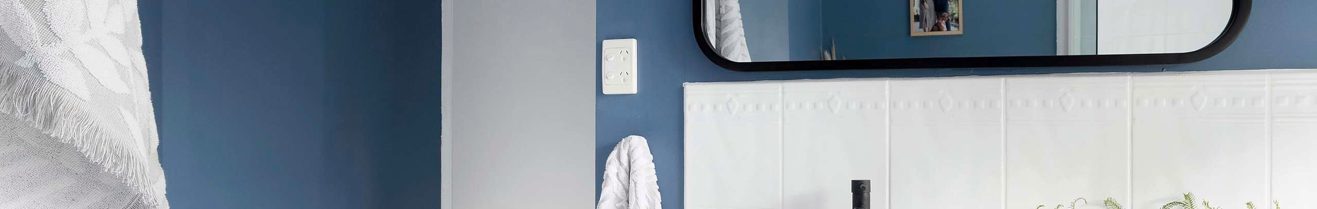 Bathroom with blue walls, white tiles, timber vanity and white cupboards.