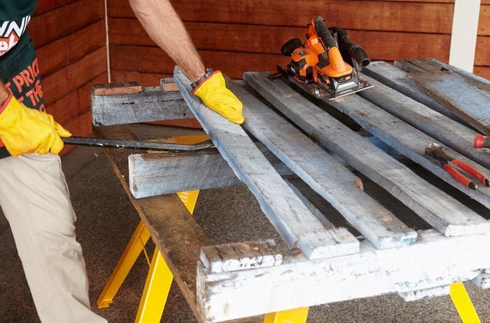 Planks of an old pallet being pried up by a Bunnings team member with a pry bar