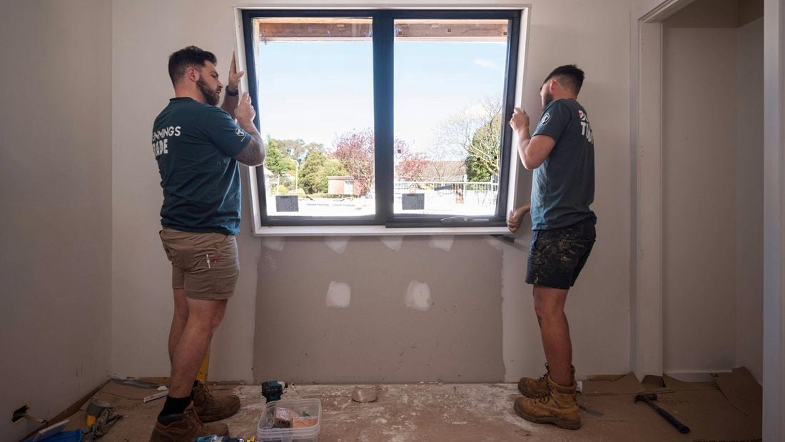 Two people installing double glazed windows inside a room
