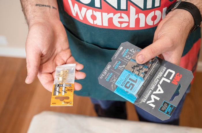 A Bunnings Team Member holding a packet of picture hooks and claw hooks