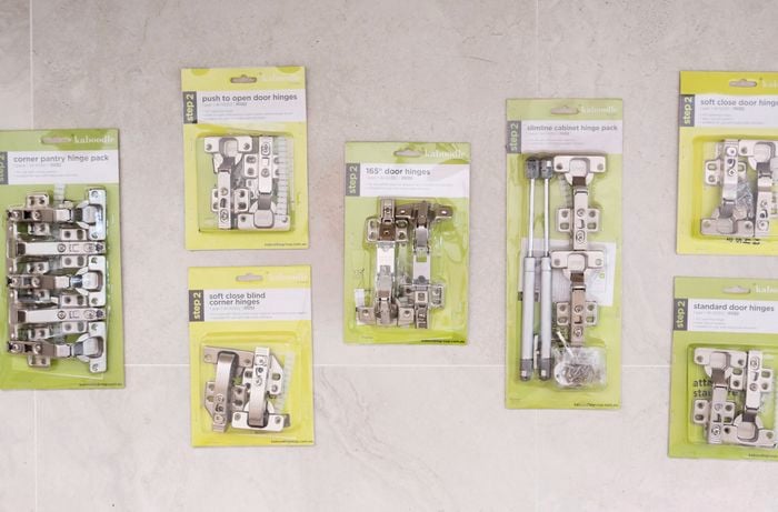 The image displays various cabinet hinges laid out on a tiled surface to help identify which hinge type to use