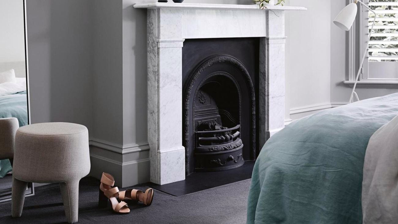 Fireplace, end of bed, mirror, in room with grey walls.