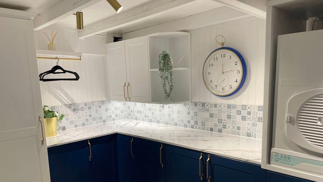 Kitchen with blue cupboards, a white stone benchtop and a clock on the wall.