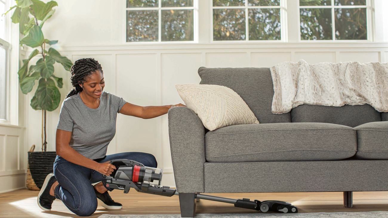 Woman vacuums underneath of couch