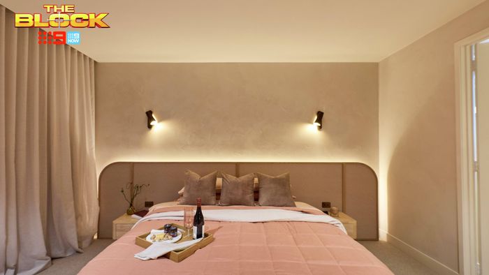 Contemporary bedroom featuring soft pink bedding, a curved upholstered bedhead, neutral walls and wall-mounted bedside lights.