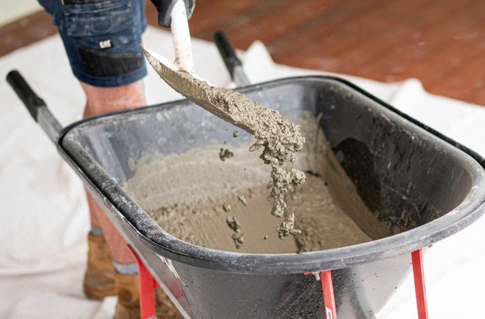 Adjust the consistency of mixed concrete in a wheelbarrow with a shovel 