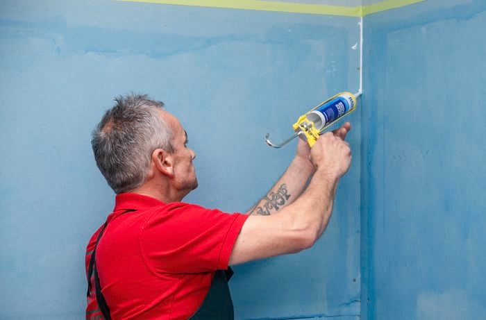 Man applying sealant to joints and corners.