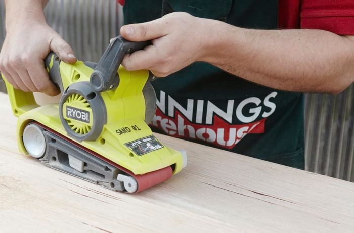 A person sanding a piece of hardwood with a belt sander