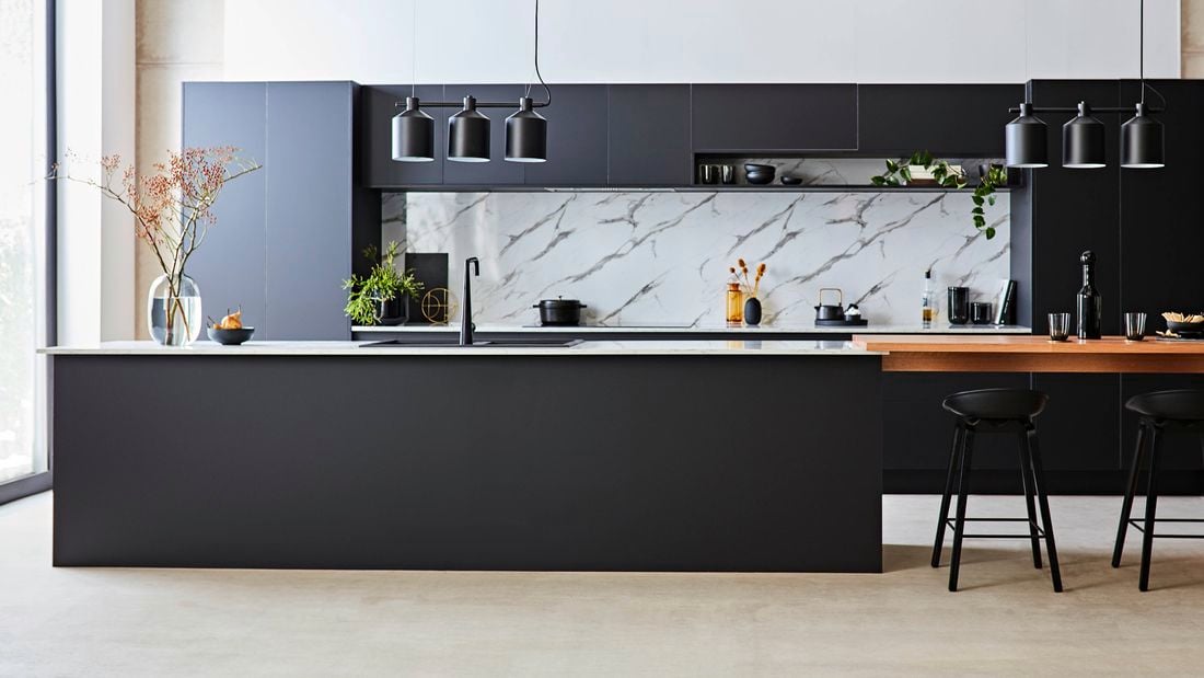 Modern kitchen featuring a matte black island bench, white marble-look splashback, black cabinetry and pendant lighting.