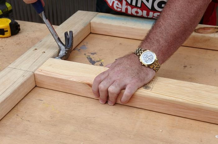 A person using a hammer to tap pine framing timber into position