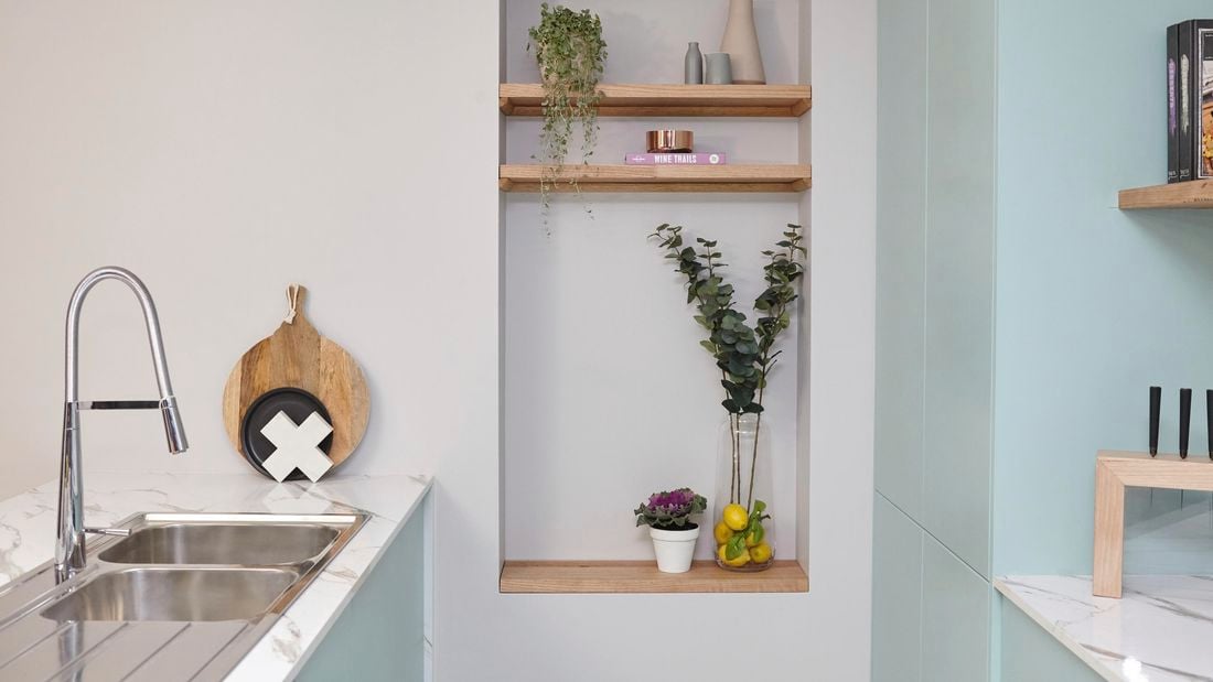Kitchen island bench and sink with platter by the wall, next to wall niche full of decorative items.