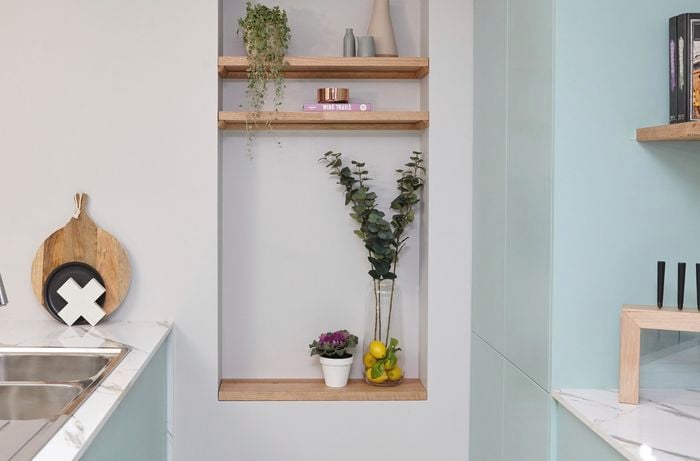 Kitchen island bench and sink with platter by the wall, next to wall niche full of decorative items.