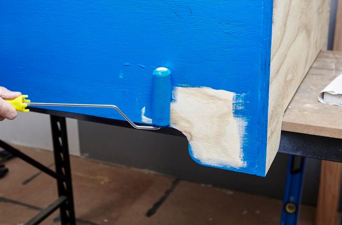 Person painting timber blue using roller brush
