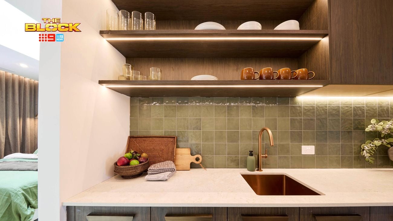 Kitchenette with green tiled backsplash, open shelves, and brass tap.
