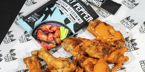 Grilled chicken wings topped with spicy sauce, served alongside a honey pepper seasoning packet.