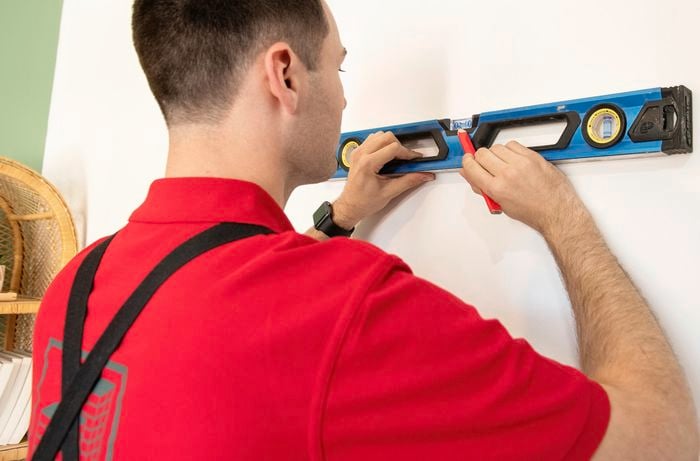 A spirit level being used to mark out positions for wall brackets on a white wall with a pencil