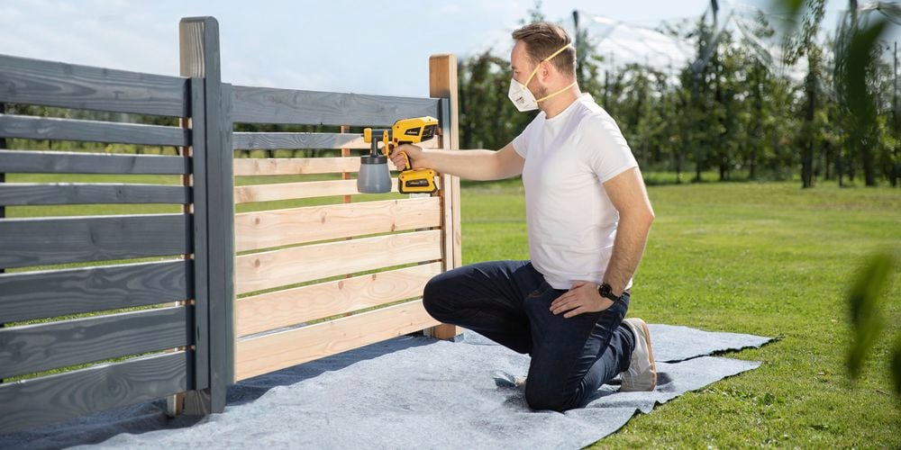 Wagner Cordless Flexio W600 spraying grey paint on a wooden fence outdoors.