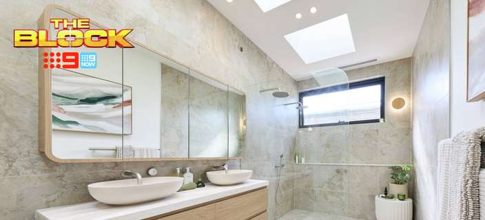 Modern bathroom with a floating timber double vanity, white vessel basins, large mirror, stone-look tiles and a spacious walk-in shower. “The Block” logo appears in the upper-left corner.
