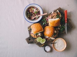 Burger rolls filled with pulled pork on a serving board with side salad