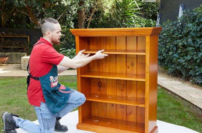 A man takes the shelves out of an old book case in preparation for sanding.​​