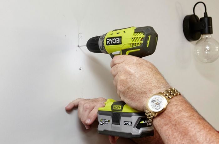 A person drilling a small hole in a plasterboard wall using a cordless drill