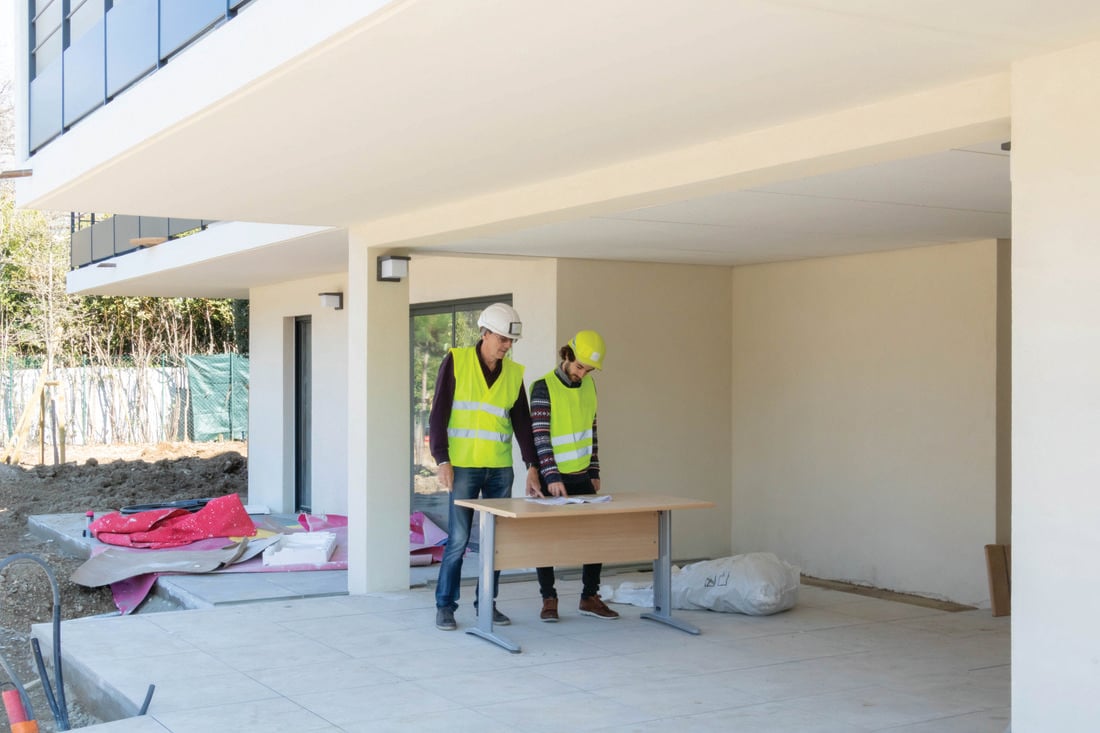 Two people in hard hats looking at a plan outside a house under construction