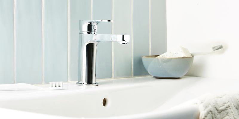 White sink with a bar of soap, a toothbrush and a hand towel on it.