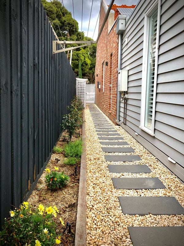 Garden down the side of a house with a garden bed and pavers surrounded by pebbles