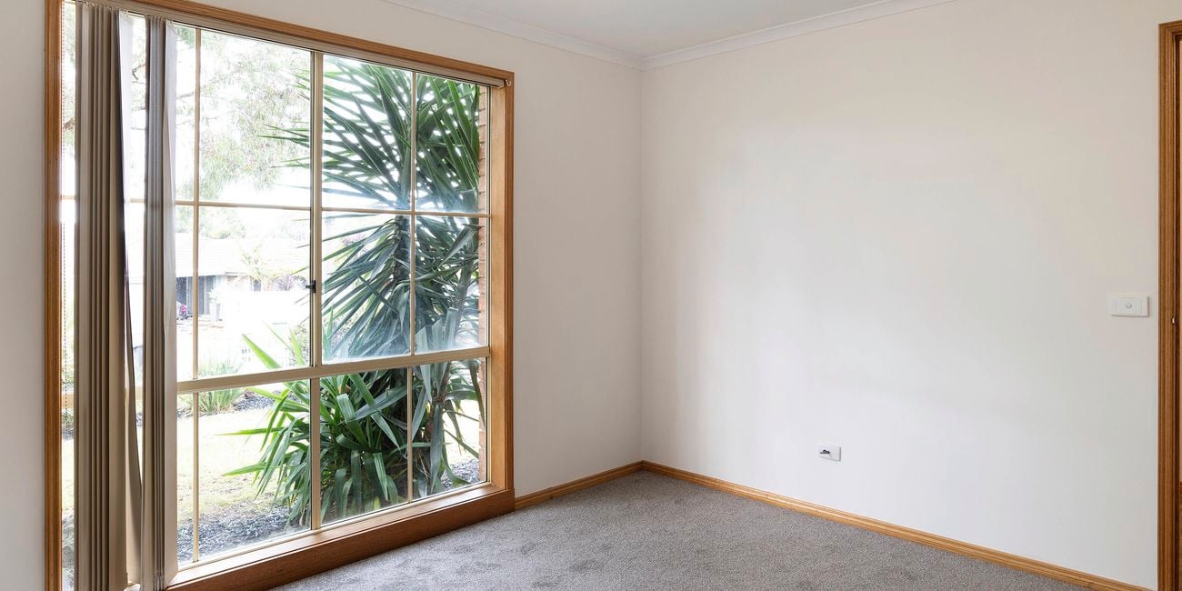 Empty master bedroom with carpet, white walls and a window facing the front of the house.