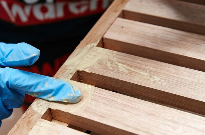 Person filling gaps in timber slat and frame with putty