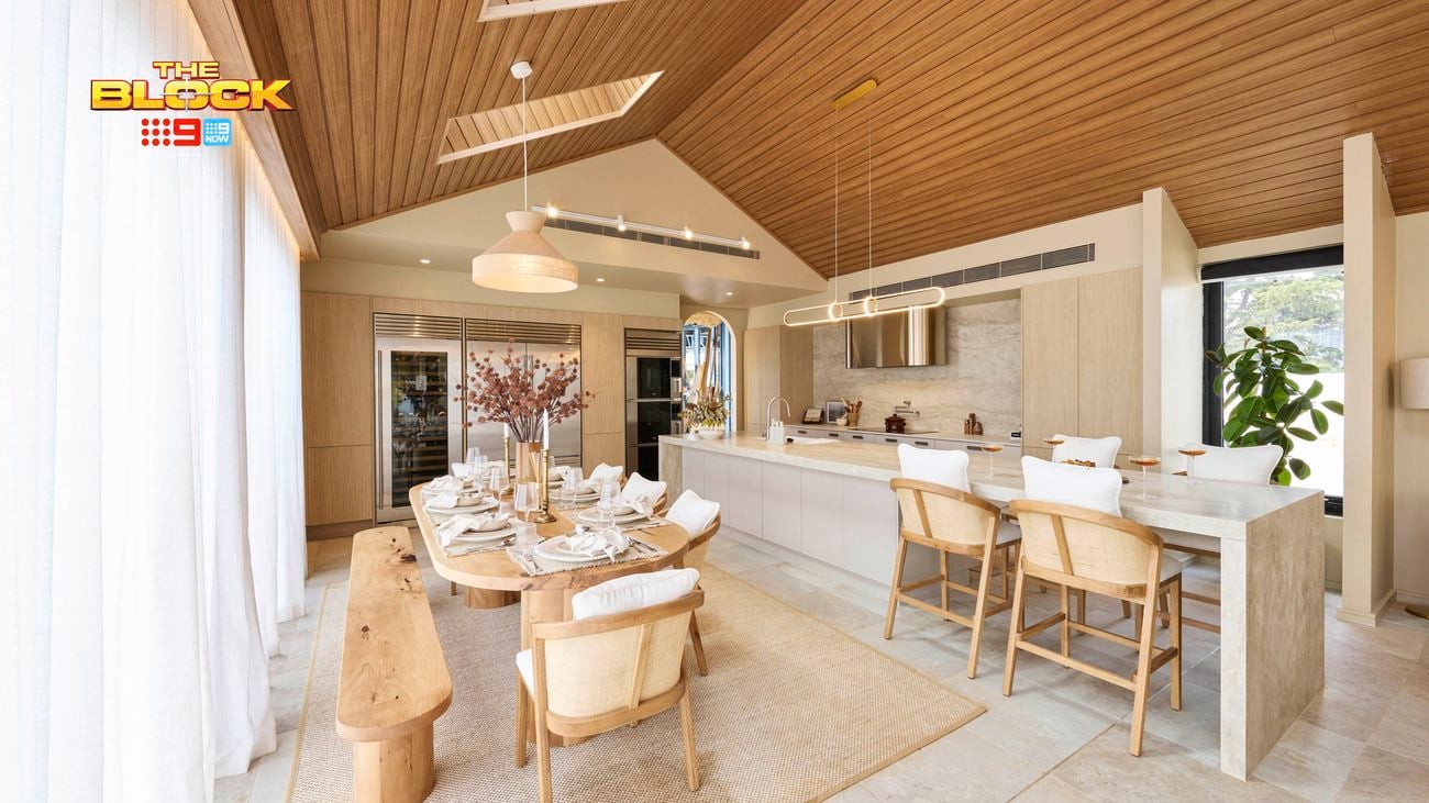 Modern open-plan kitchen and dining area with wooden ceiling, stone floor, large windows, a set dining table, and a marble island with stools.