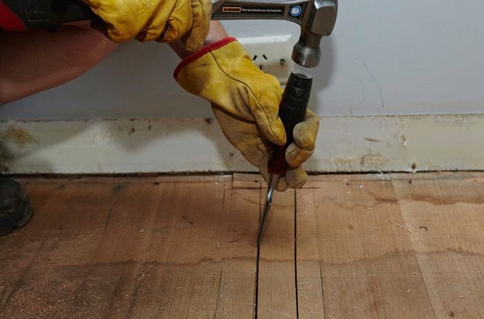 Close up of a person hammering a chisel in between two floorboards